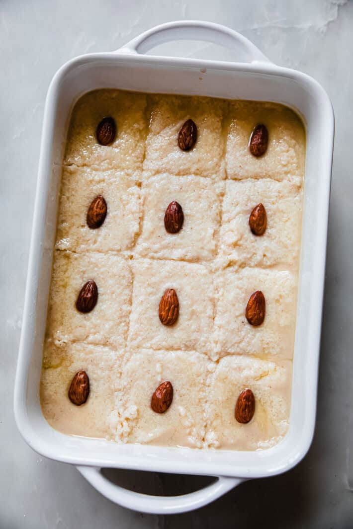 basbousa batter in dish, scored and topped with soaked almond