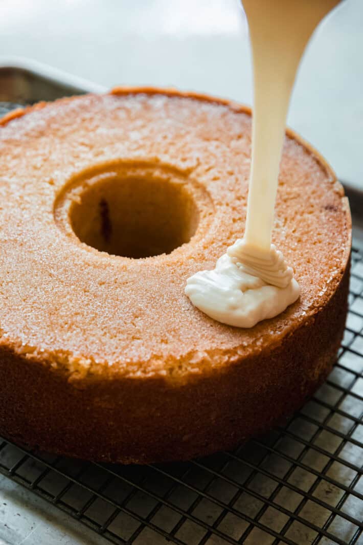 pouring glaze on top of slightly cooled cake before covering in toasted coconut flakes