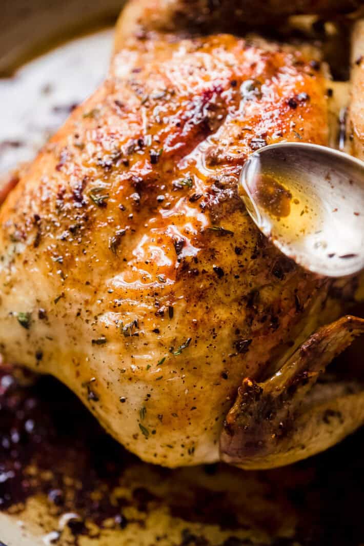 hand with spoon basting roasted chicken in pan