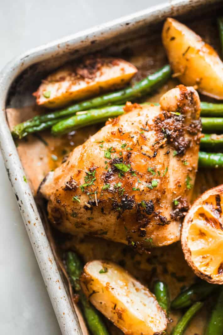 roasted chicken thigh with green beans and rosemary potatoes with lemon wedge