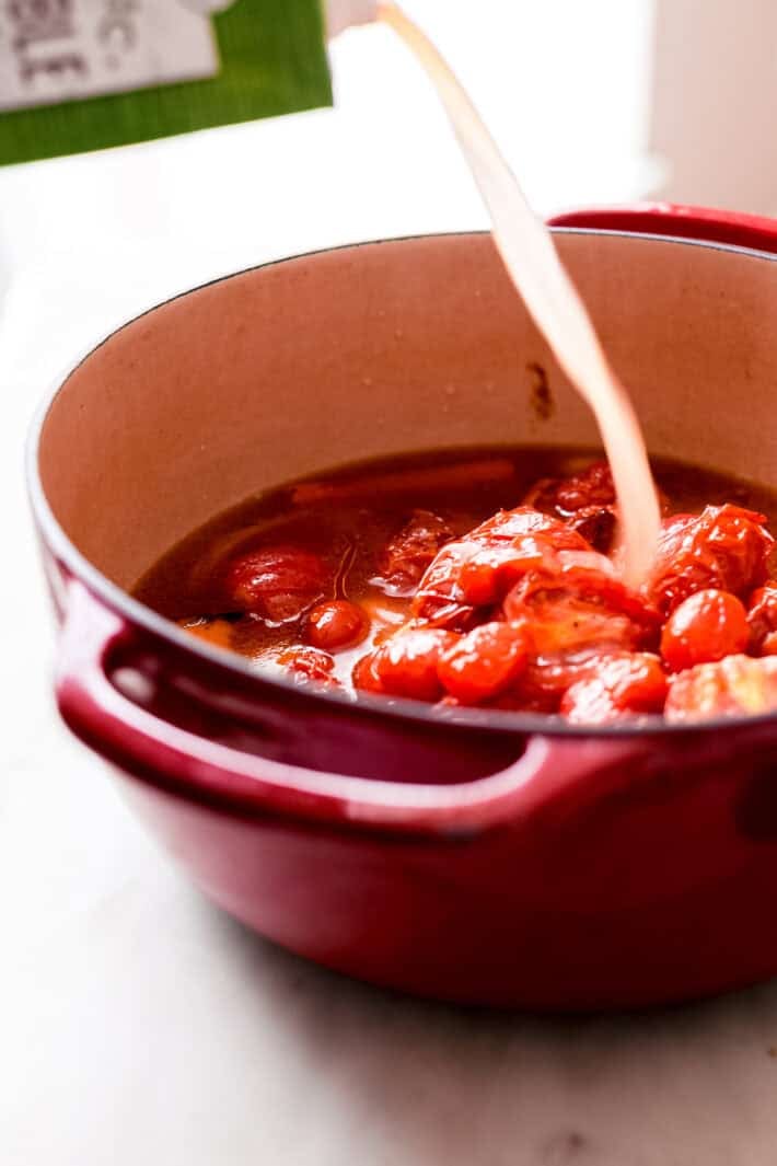 pouring vegetable stock into a potful of roasted vegetables