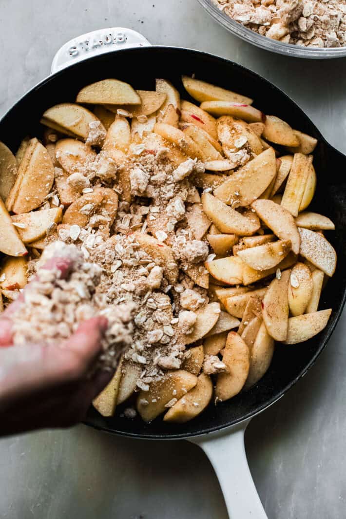 hand sprinkling crumb topping on apple slices