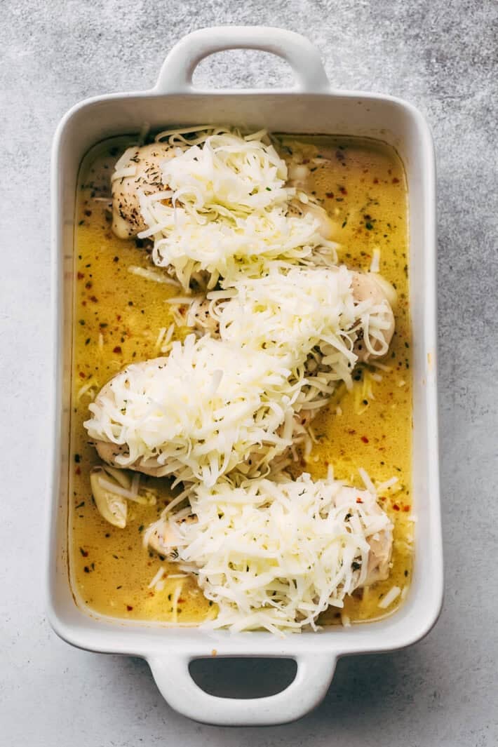 half-baked chicken topped with shredded mozzarella cheese in white baking dish