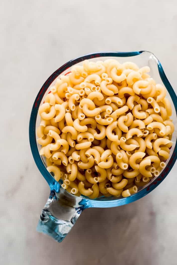 measuring cup filled with dry elbow macaroni on white marble