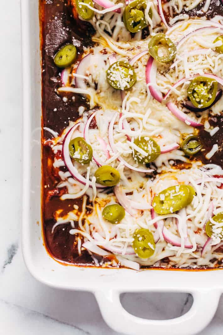 bbq sauce with cooked chicken topped with shredded mozzarella cheese, pickled jalapeños, and raw red onions ready to go in the oven