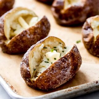 freshly baked potatoes on a sheet pan with butter and chives