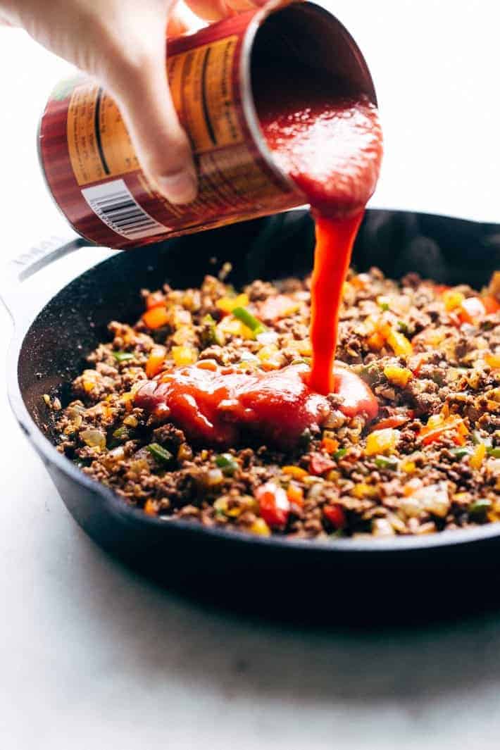 pouring tomato sauce into skillet with chili ingredients