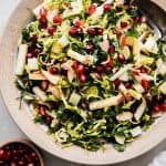 shaved brussels sprout salad in rimmed bowl with apples and pomegranate arils