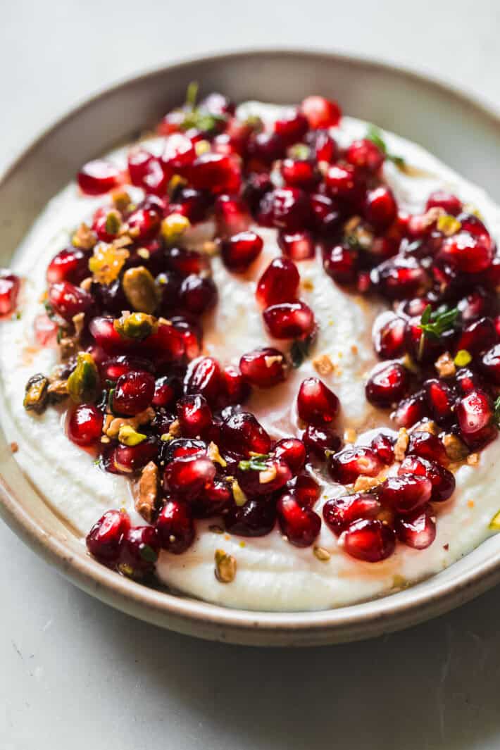 dip in bowl topped with pistachios, thyme, and pomegranate