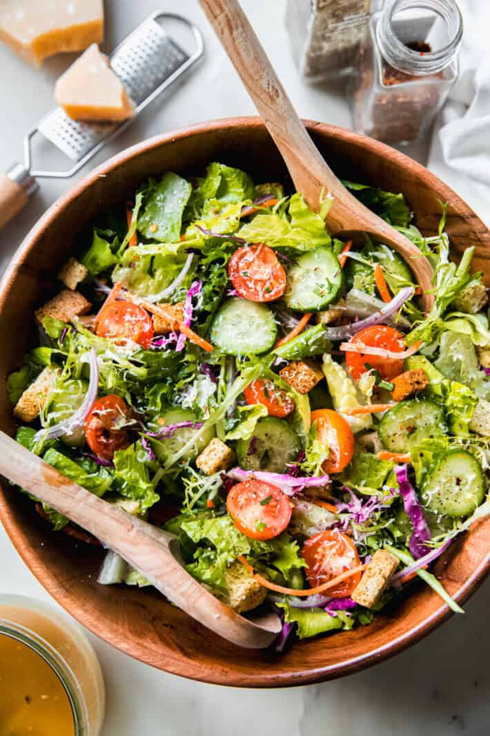salad in bowl with wooden spoons and ingredients surrounding