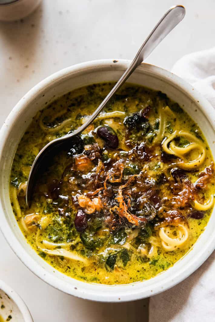 soup in bowl with spoon, mint oil, and onions