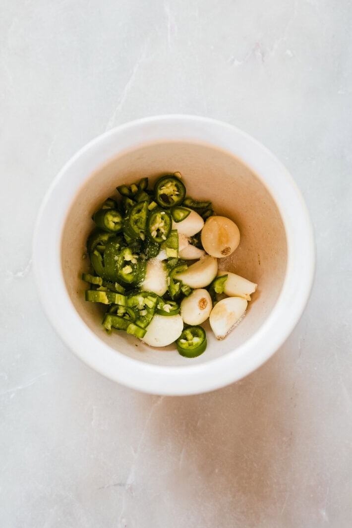 garlic cloves and serrano peppers with salt in mortar