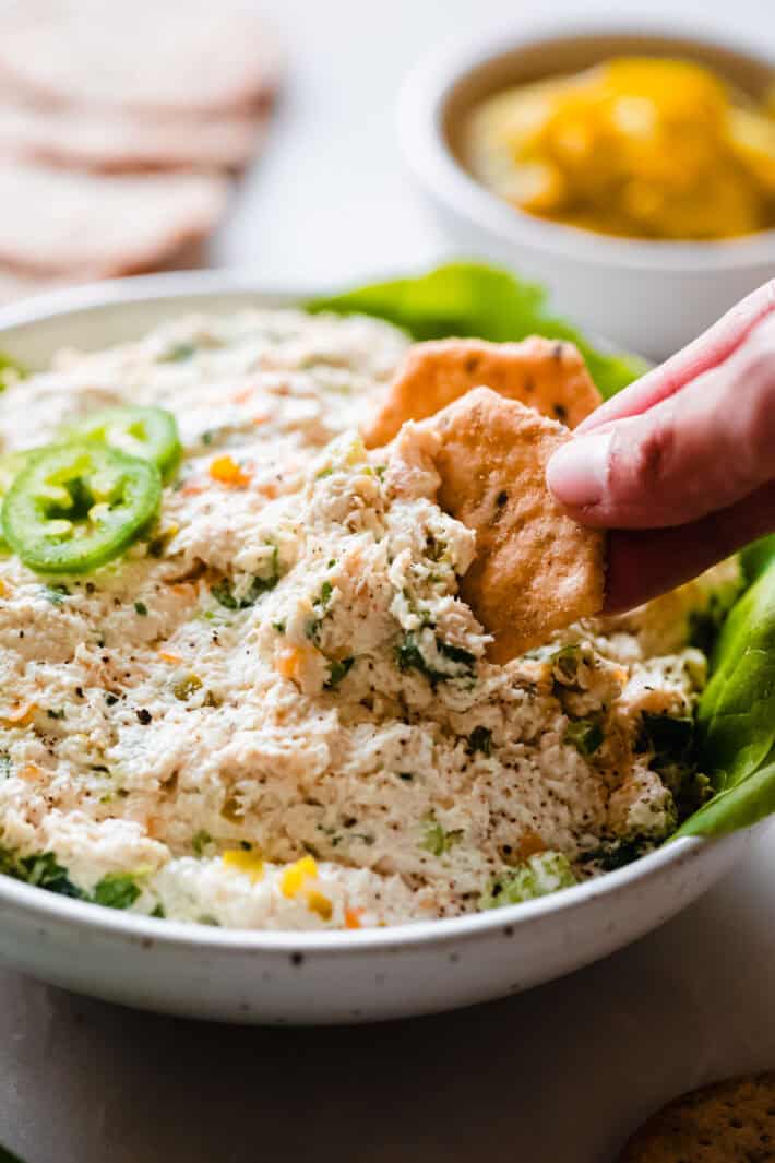 hand lifting cracker with chicken salad from bowl