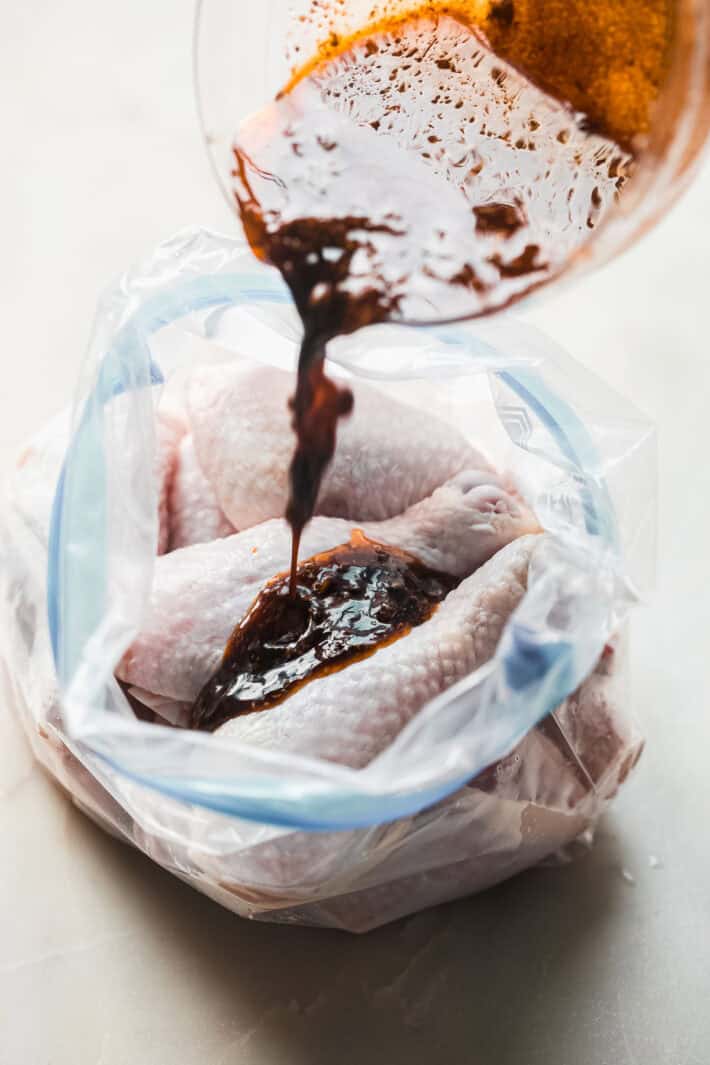 pouring marinade over raw chicken drumsticks