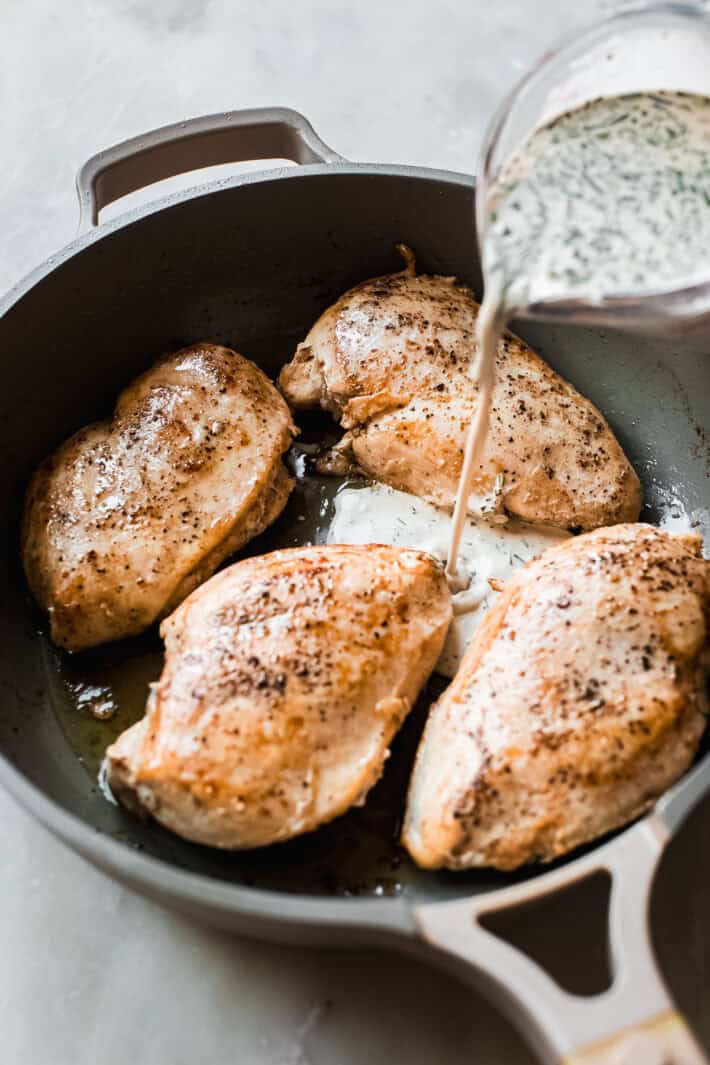 pouring creamy peppercorn sauce over seared chicken