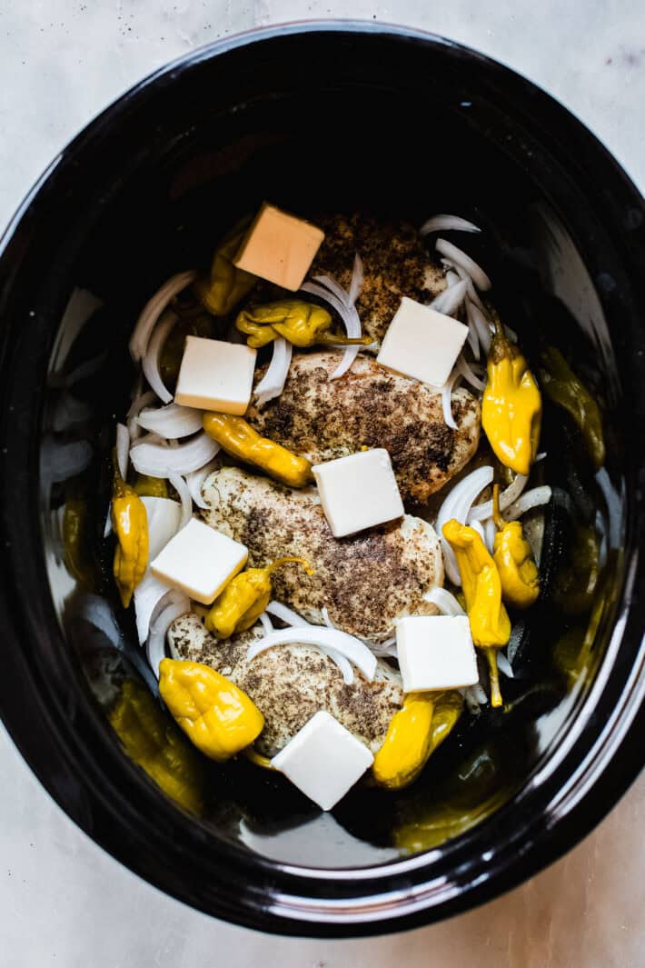 uncooked chicken with butter pats and sliced onions in crock pot before cooking